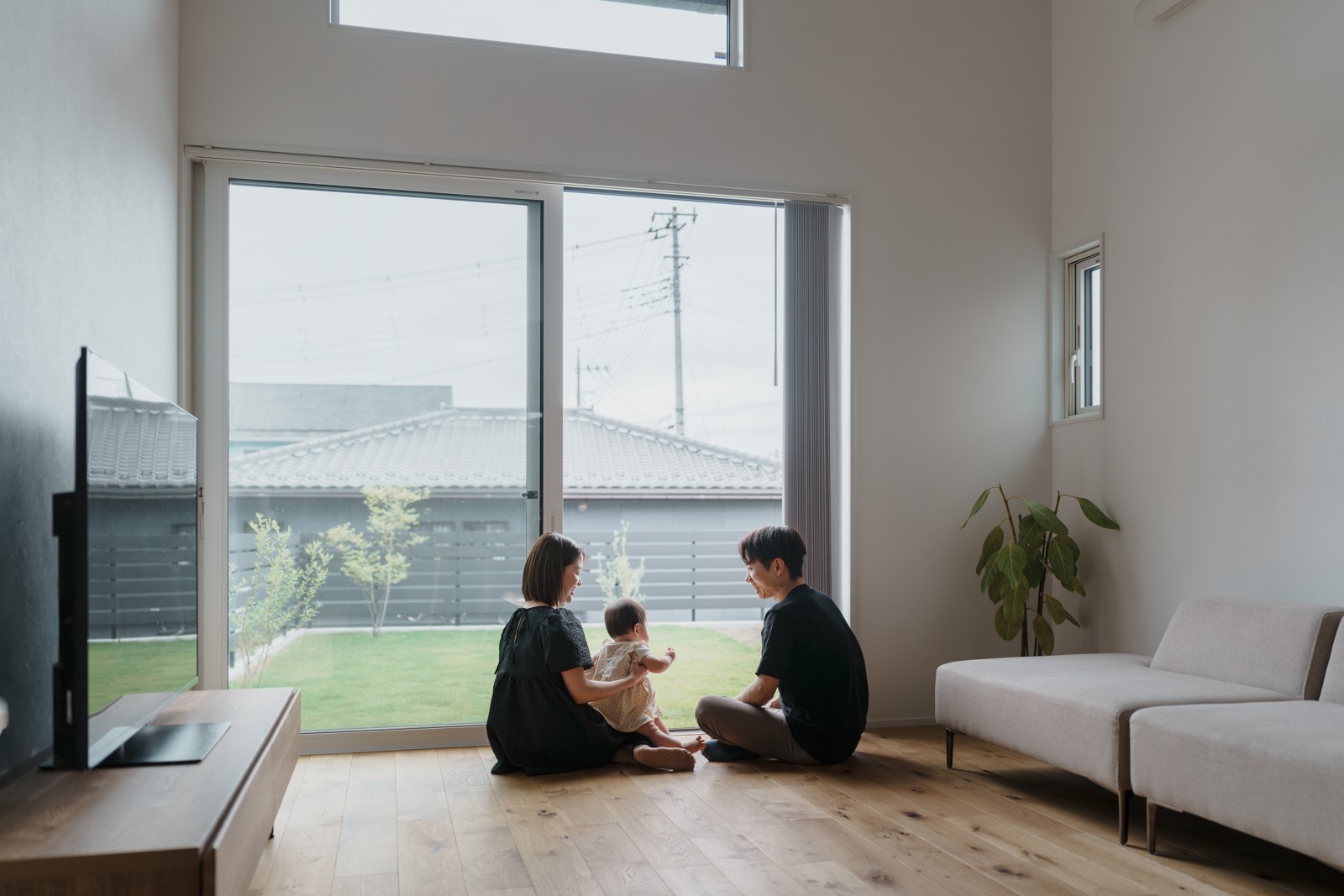 大きな窓からは庭の緑をのぞみ、吹き抜けから柔らかな光が注ぐ住まい。白を基調としたシンプルな空間に木のぬくもりと黒のアクセントをひとさじ。